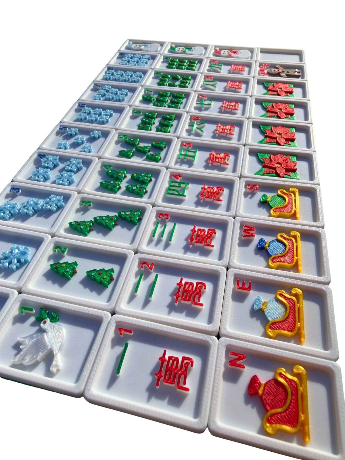 A set of american mahjong tiles arranged in a grid on a white background. The tiles feature various designs including green pine trees, red Chinese characters, blue floral motifs, and colorful animal and landscape tiles.