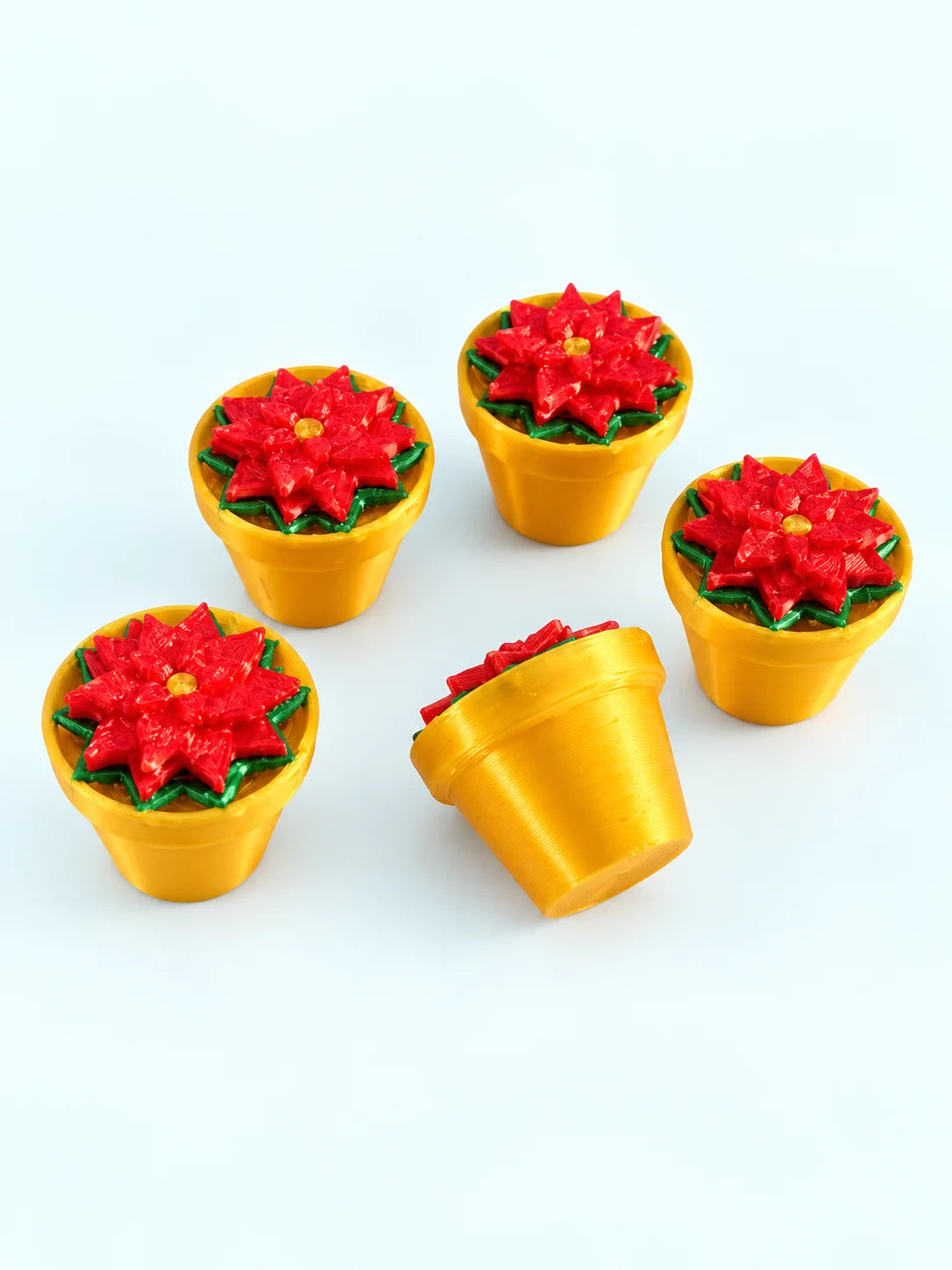 Five poinsettia mahjong trinkets with red flowers in gold pots, one tipped on its side, 3D printed by Spools