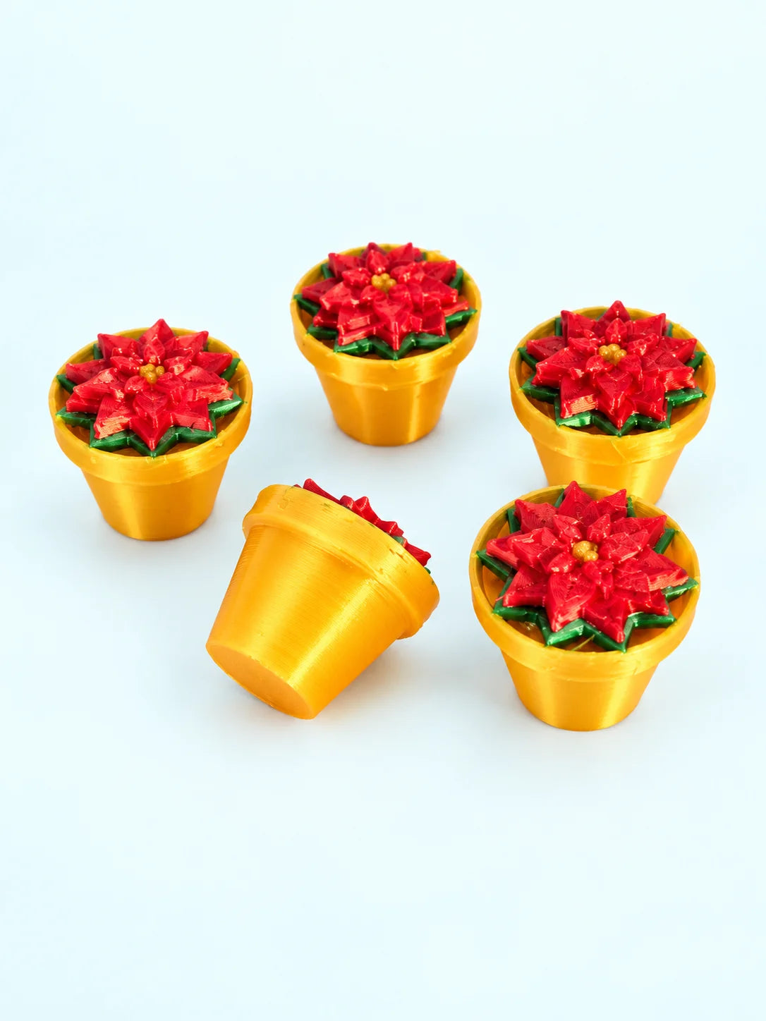 Poinsettia mahjong trinkets with red petals, green leaves, and gold pots, 3D printed by Spools