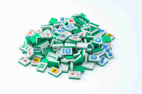 A pile of green and white mahjong tiles with various symbols and illustrations, photographed on a clean white background.