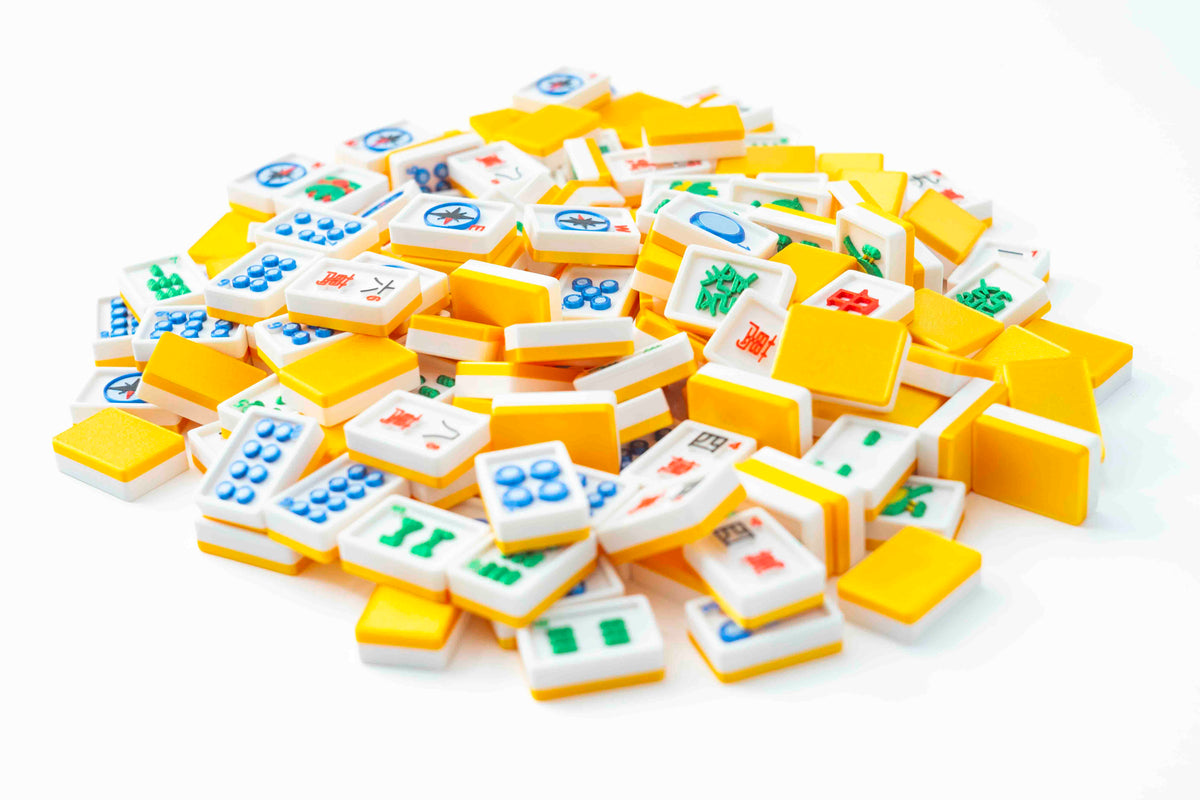 A pile of miniature Mahjong tiles in yellow, white, blue, green, and red, arranged on a clean white background.