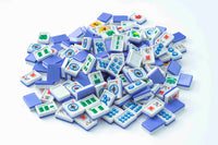 A pile of Mahjong tiles on a plain white background, showing the back and front views of the tiles. The back of the tiles is a solid medium blue, while the front faces are white with various colored Chinese characters and symbols.