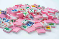 A pile of miniature pink and white Mahjong tiles with colorful Chinese characters and symbols, arranged on a clean white background.