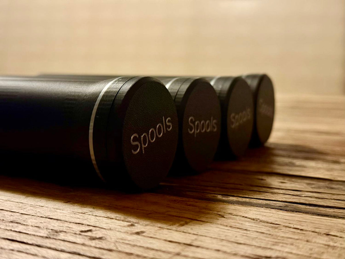 Four black cylindrical Aero-Poker chip tubes, each stamped Spools, lie side by side on a wood table.