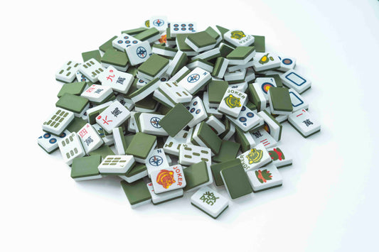 A pile of miniature mahjong tiles with green backs and white fronts printed with various Chinese characters and symbols, set against a plain white background.