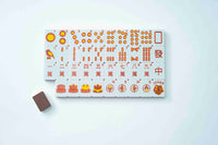 A set of Mahjong tiles arranged in a grid on a white background, with a single brown eraser placed to the left. The tiles are white with orange and red printed symbols and characters, and one tile shows the word 'JOKER'.