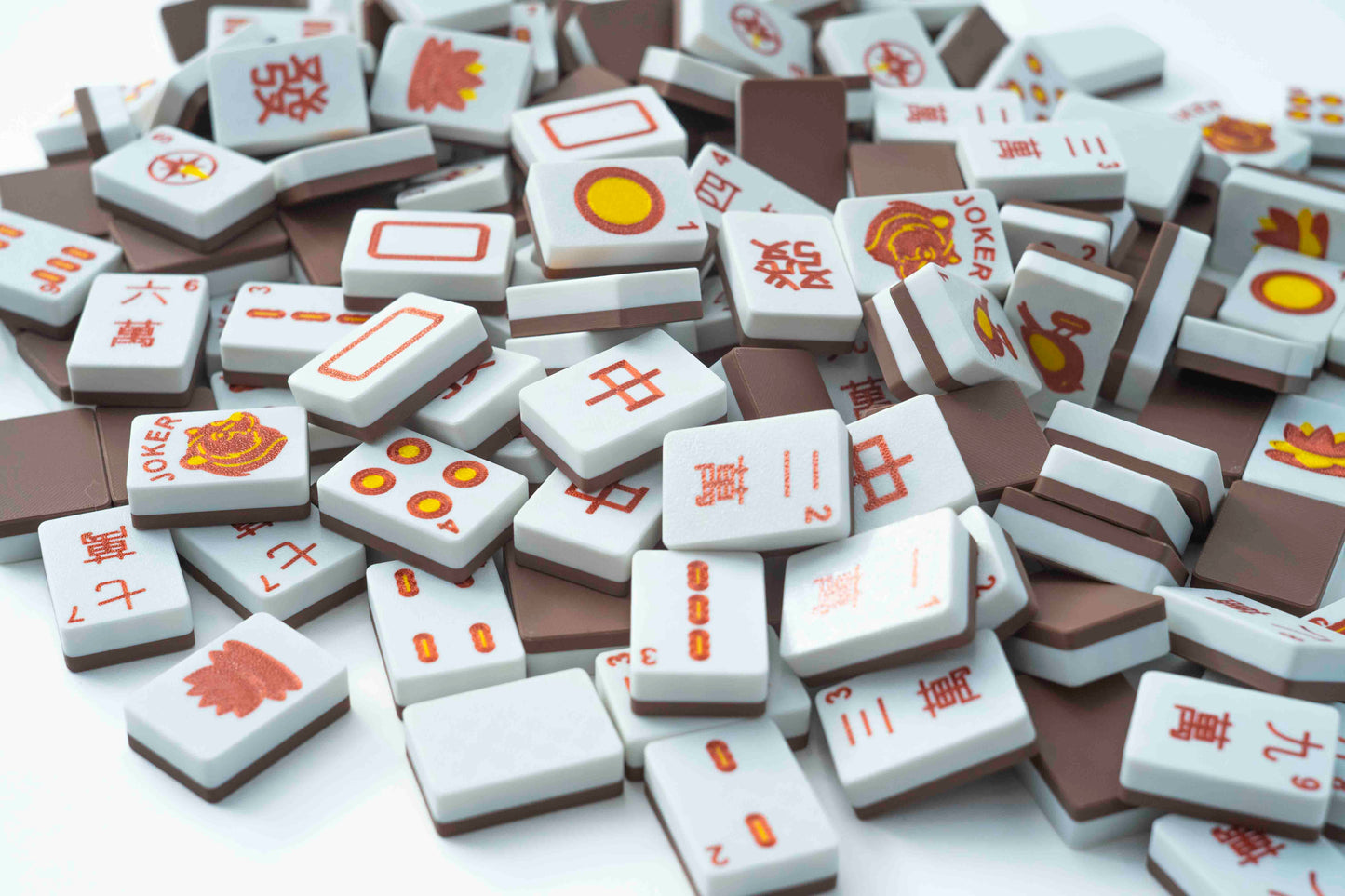 A pile of miniature mahjong tiles with Chinese characters and red-orange symbols on a white background.