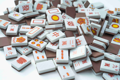 A pile of miniature mahjong tiles with Chinese characters and red-orange symbols on a white background.