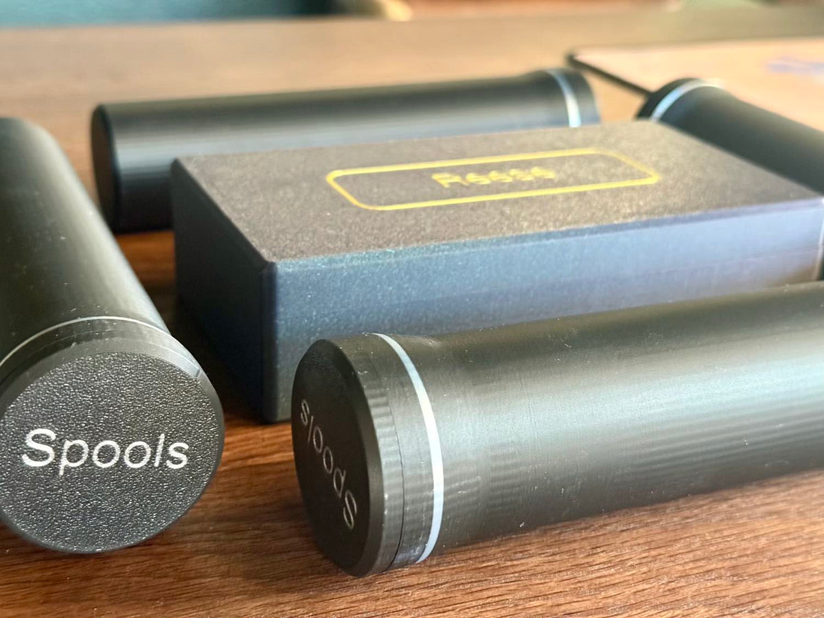 Aero-Poker chip tubes and their dark storage box cluster together on a wood table, one tube's Spools cap upside down.