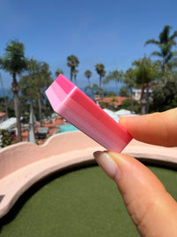Close-up of a pink Flamingo mahjong tile held poolside with palm trees behind