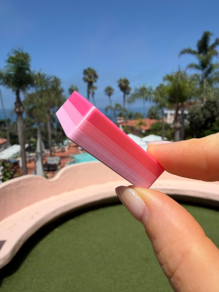 Close-up of a pink Flamingo mahjong tile held poolside with palm trees behind