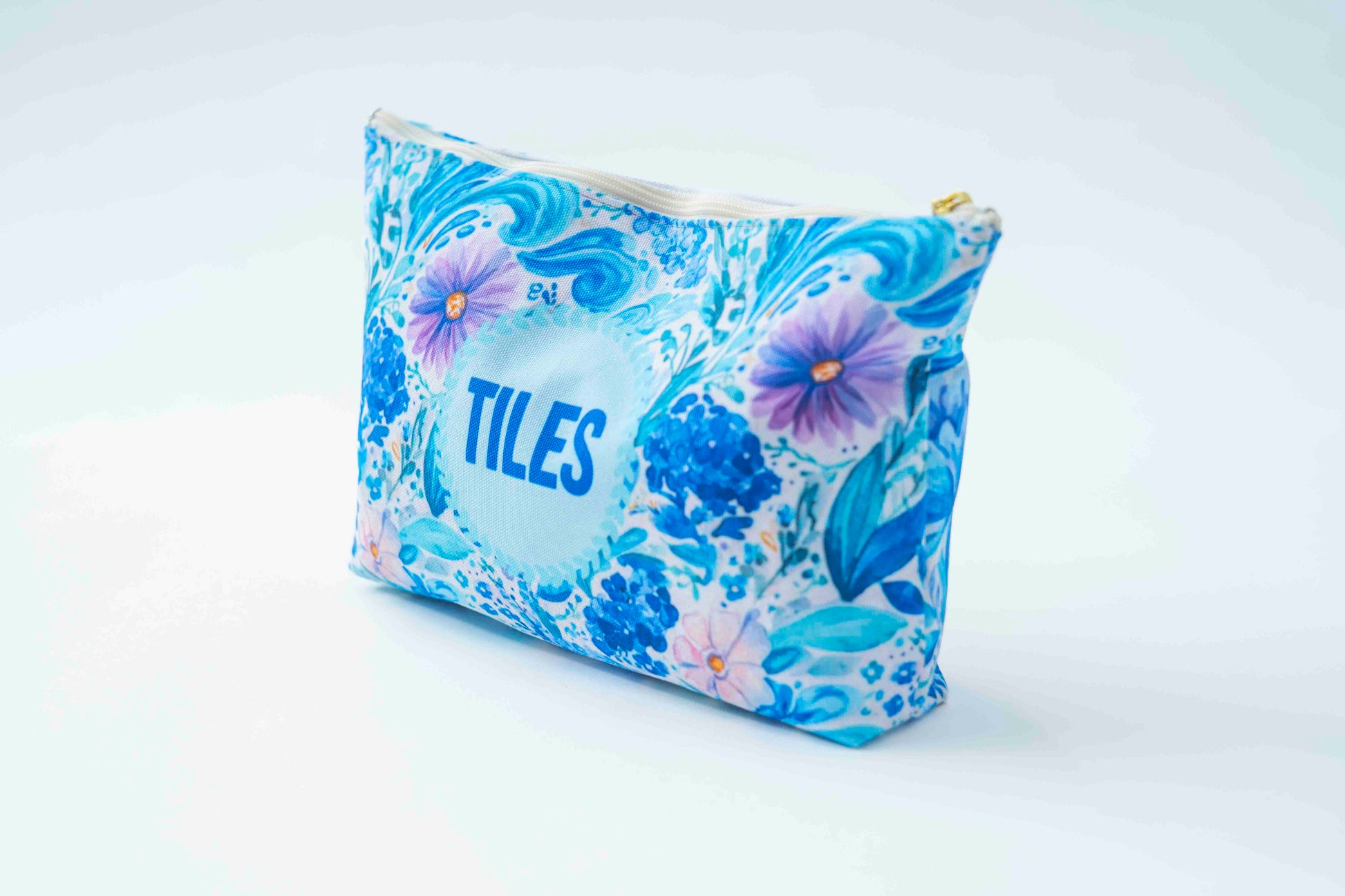 A zippered cosmetic pouch featuring a blue and white Japanese wave pattern with purple flowers and the word 'TILES' printed in blue on the front, set against a clean white background.