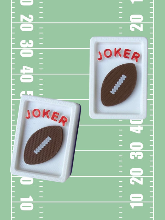 Two small white rectangular inserts with brown football-shaped pieces and red text reading "JOKER," shown on a green field-style background with white yard-line markings.