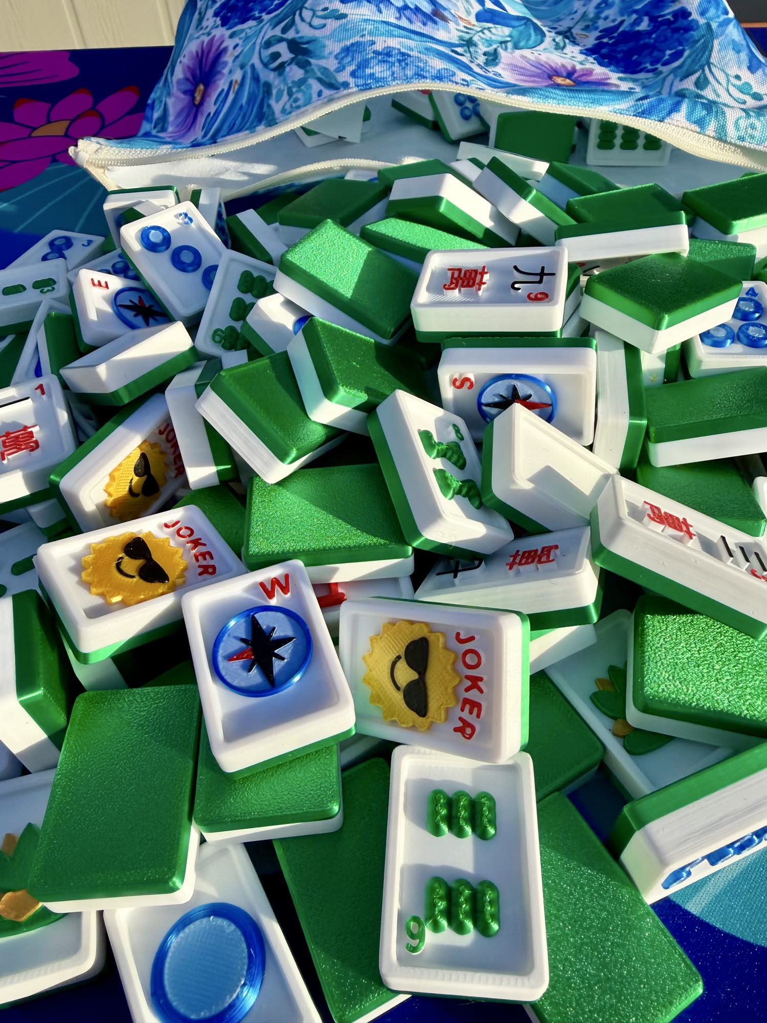 Green Travel Mahjong Tiles - 3D spill from an open floral-blue pouch, tiles piled close together.