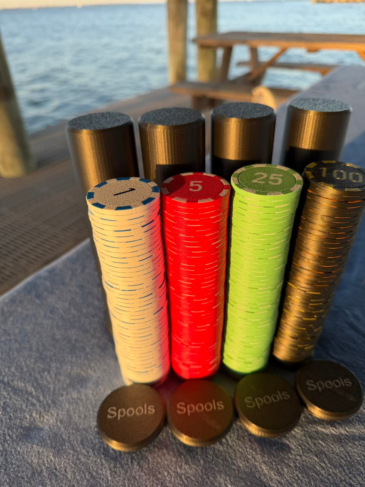 Aero-Poker chip tubes stand behind cream, red, green, and gold chip stacks on a dock table beside open water.