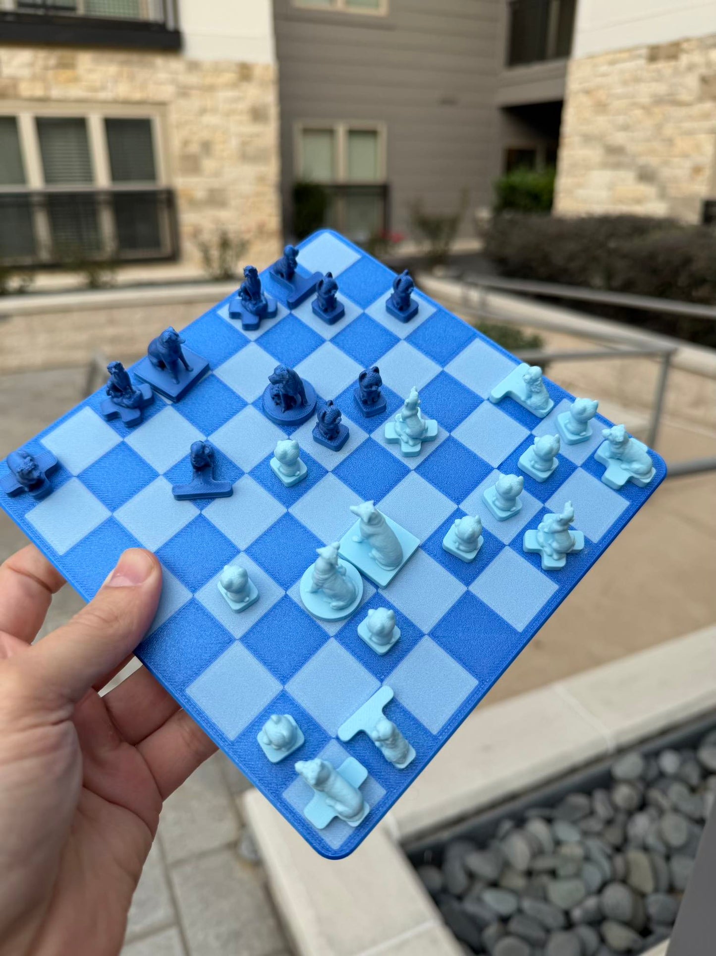A hand tilts the magnetic Fridge Chess board outdoors, dog-shaped pieces holding fast to the checkered squares at an angle.