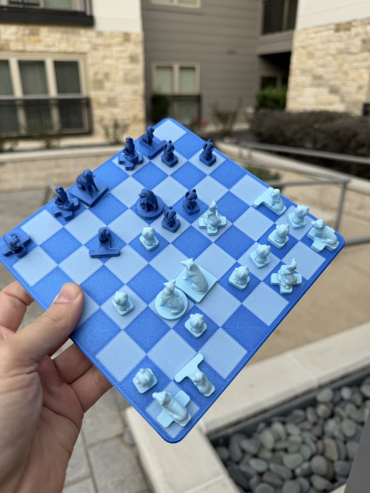 A hand tilts the magnetic Fridge Chess board outdoors, dog-shaped pieces holding fast to the checkered squares at an angle.