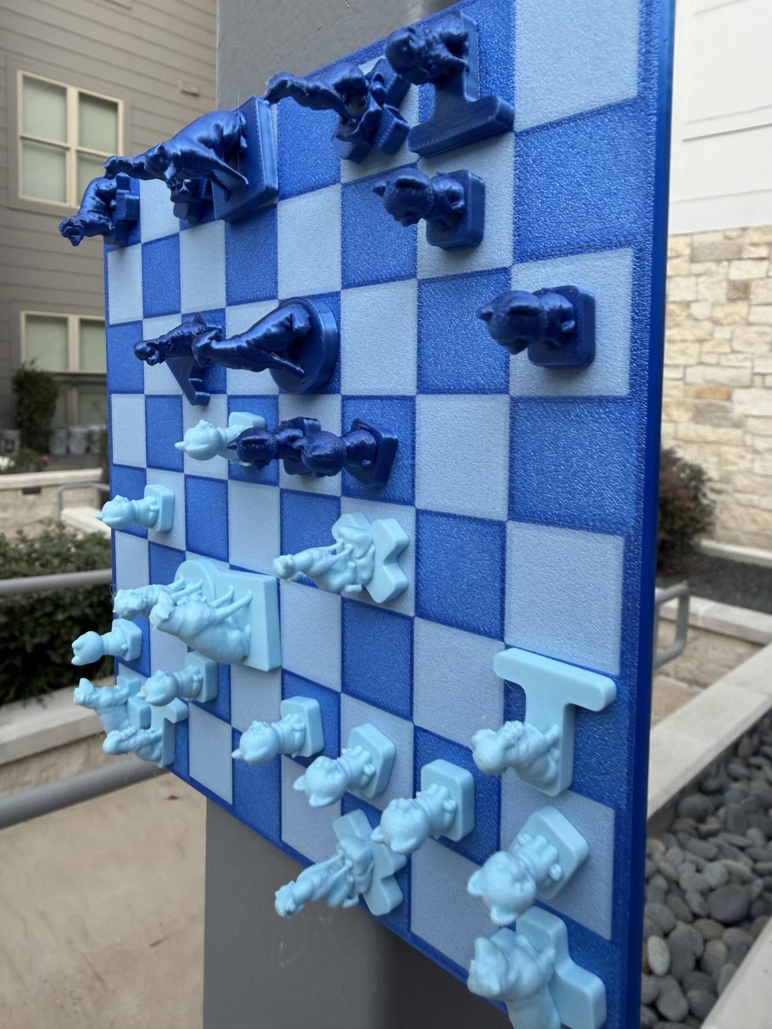 Dark and light blue dog-shaped chess pieces cling magnetically to a vertical board mounted on an outdoor pillar.