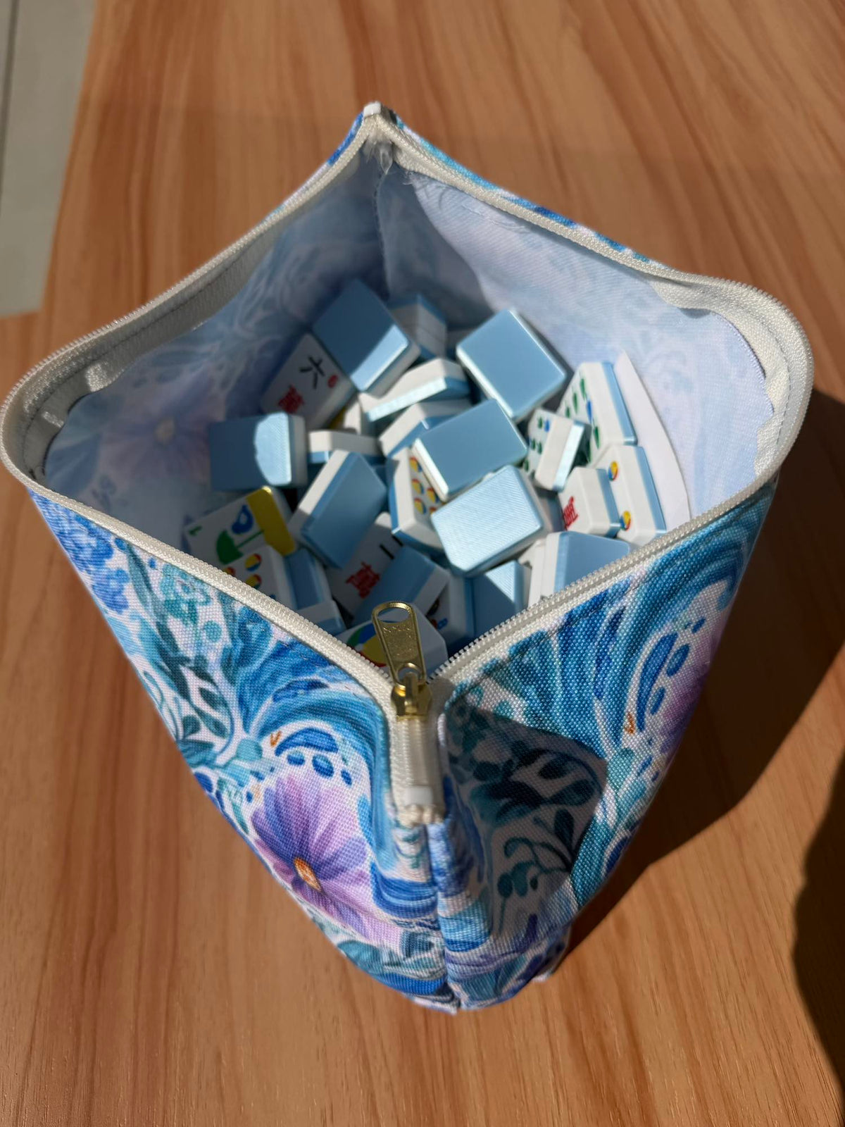 Blue and purple floral pouch unzipped and open, revealing light blue mahjong tiles packed inside