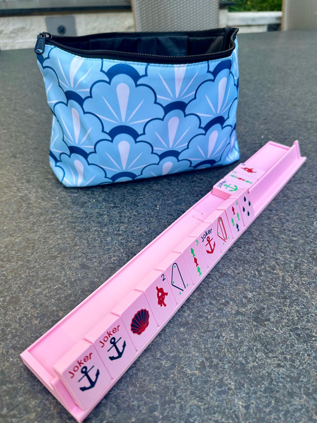 Pink floating mahjong rack with nautical-themed tiles displayed in front of a blue scallop-patterned carrying bag