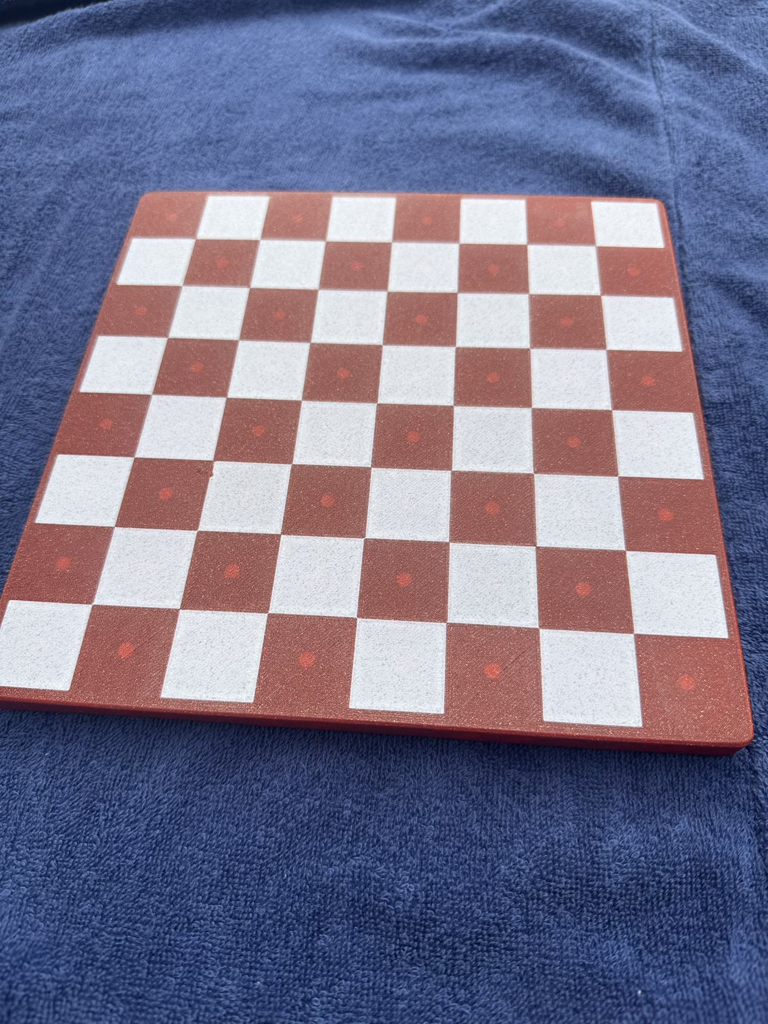 An empty brick-red board with dotted squares shows the fourth Dachshund Travel Chess colorway on a purple towel.