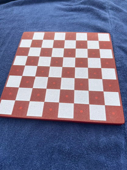 An empty brick-red board with dotted squares shows the fourth Dachshund Travel Chess colorway on a purple towel.