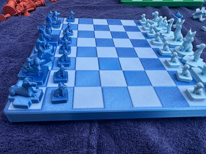 A blue Dachshund Travel Chess board holds its dog-shaped pieces mid-setup, orange pieces and a green rack blurred behind.