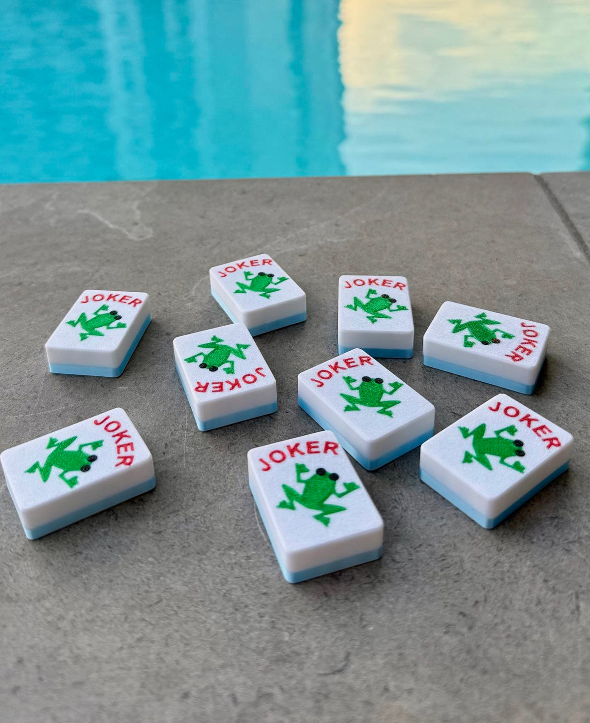 Custom Jokers - Frogs tiles lie scattered across poolside concrete, green frogs facing every direction.