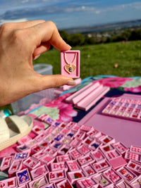 A hand holds a pink Flamingo mahjong tile at a park picnic, more tiles on the blanket below