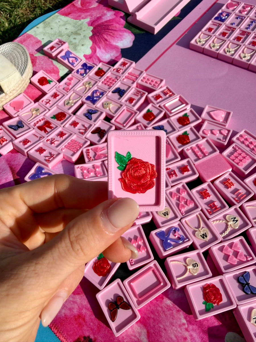 A hand holds a pink Flamingo flower tile with a red rose over a blanket of tiles