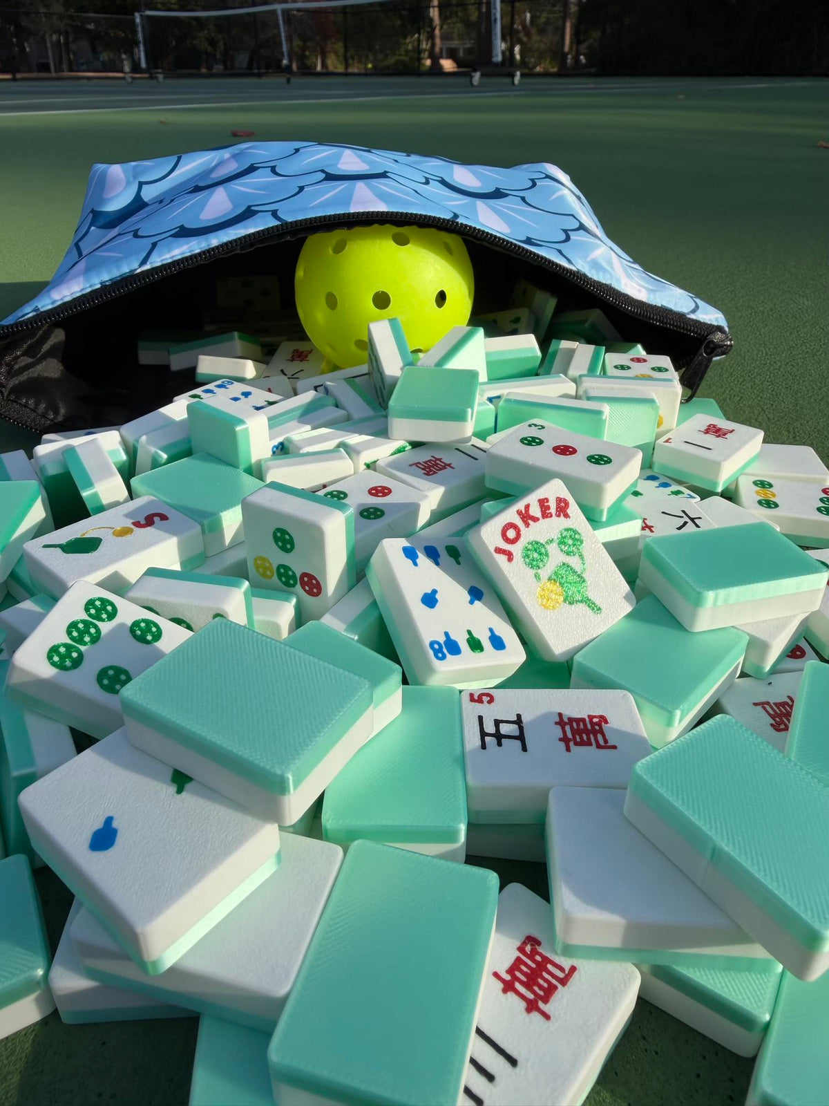 A pickleball peeks from the tile pouch, mint Travel Mahjong Tiles bearing a pickleball-themed Joker tile beside it.