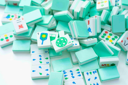 A pile of miniature Mahjong tiles in mint green and white, showing various playing card faces and tile patterns on a clean white background.
