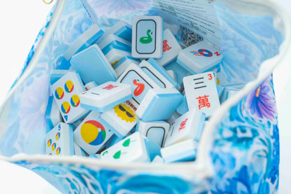 A close-up of Mahjong tiles inside a blue and white patterned zippered bag, showing the back and front faces of several tiles.