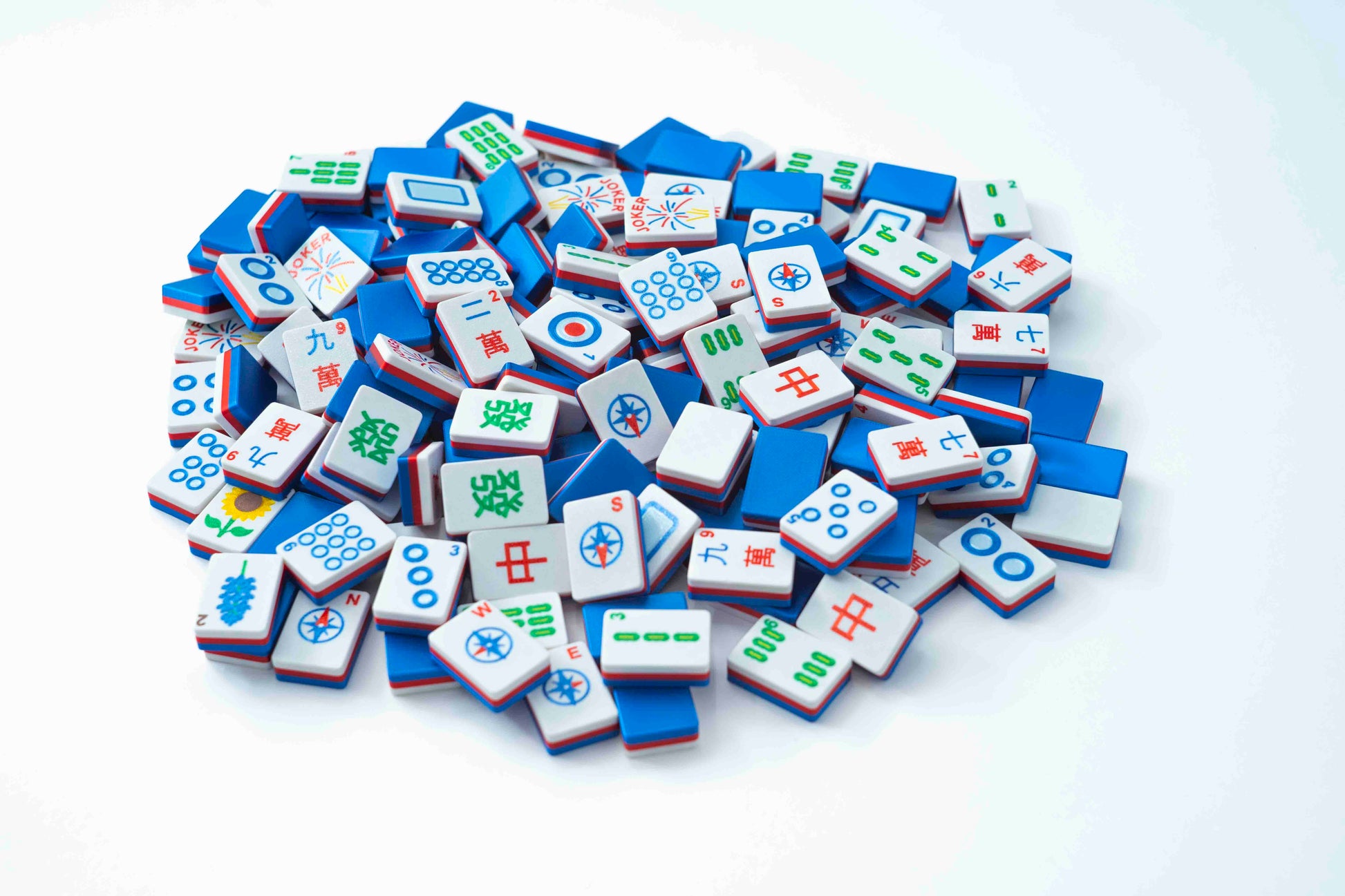 A pile of miniature Mahjong tiles in blue, white, and red, scattered on a clean white background.