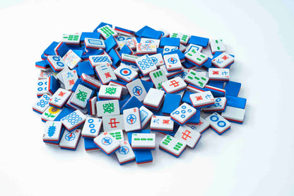 A pile of miniature Mahjong tiles in blue, white, and red, scattered on a clean white background.