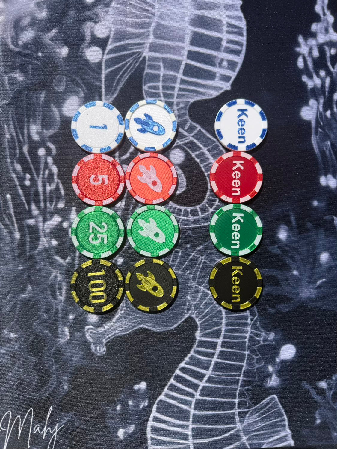 A set of 15 poker chips arranged in two columns on a dark, stylized background featuring a white seahorse illustration. The left column contains blue, red, green, and black chips with numbers 1, 5, 25, and 100.