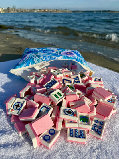 Pink Travel Mahjong Tiles - 3D spill from their pouch onto a white towel, a bay and distant shoreline behind.