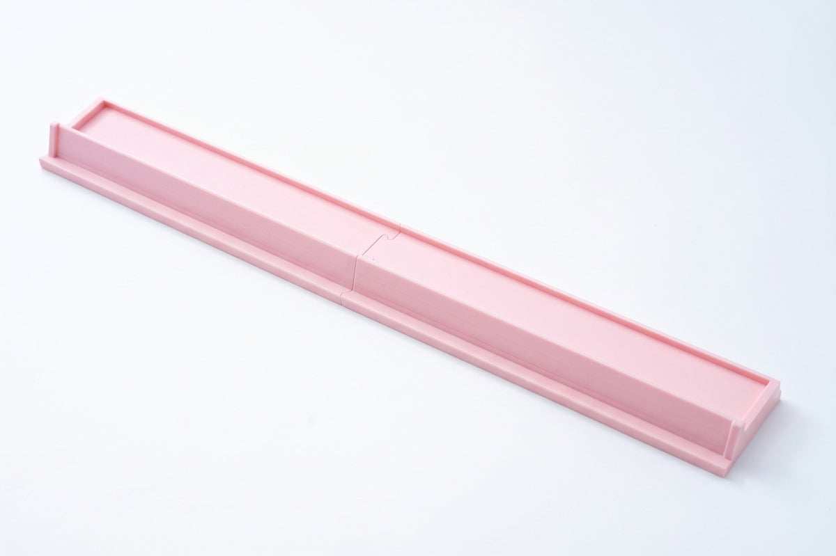 A long, narrow pink plastic tray or mold with a segmented design, shown diagonally on a clean white background.
