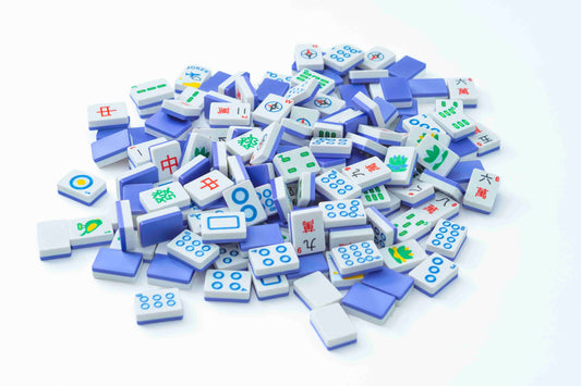 A pile of miniature Mahjong tiles in white and blue, featuring various Chinese game symbols and characters, arranged on a clean white background.
