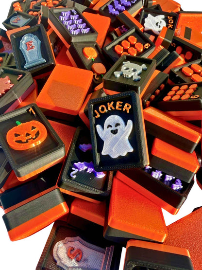 A pile of Halloween-themed Travel Mahjong Tiles featuring orange and black tiles with various spooky designs including jack-o'-lanterns, ghosts, skulls, tombstones, and jokers