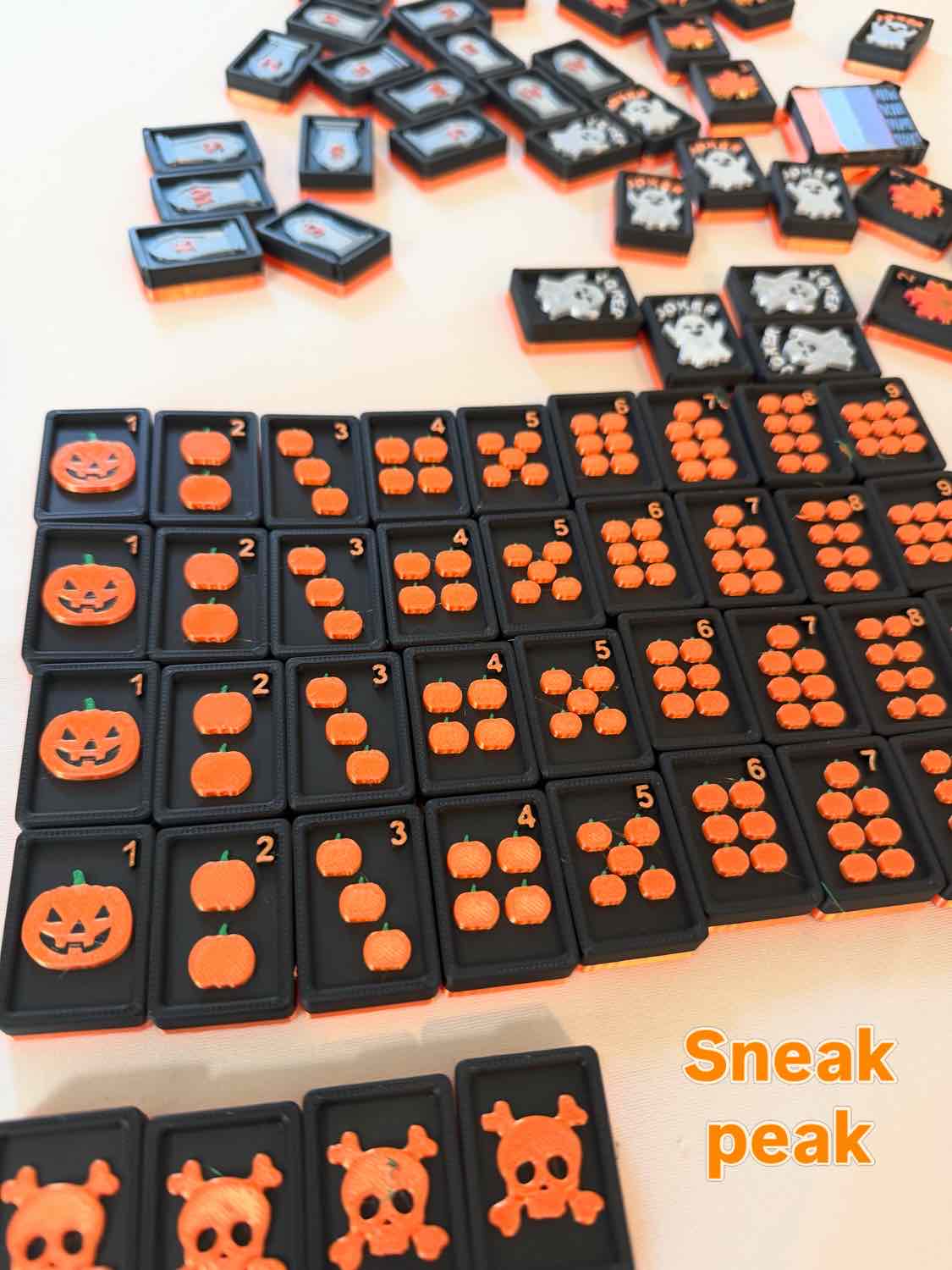 A set of black rectangular counting tiles with orange Halloween-themed designs, including pumpkins, skulls, and faces, arranged on a light surface. The text 'Sneak peak' appears in the bottom right corner.