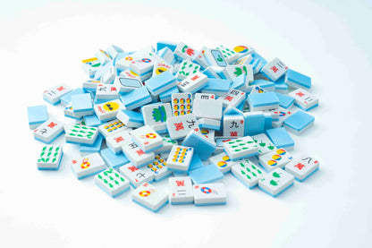 A pile of small white and light blue tiles with colorful Mahjong tiles and symbols, photographed on a clean white background.