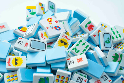 A pile of Mahjong tiles with white backs and colorful printed symbols, including Joker faces and Chinese characters, photographed on a light background.