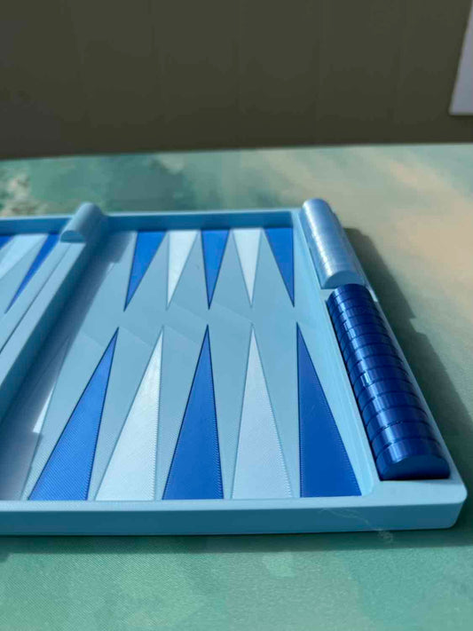 A blue and white backgammon board game set with a single rolled die visible on a green tabletop.