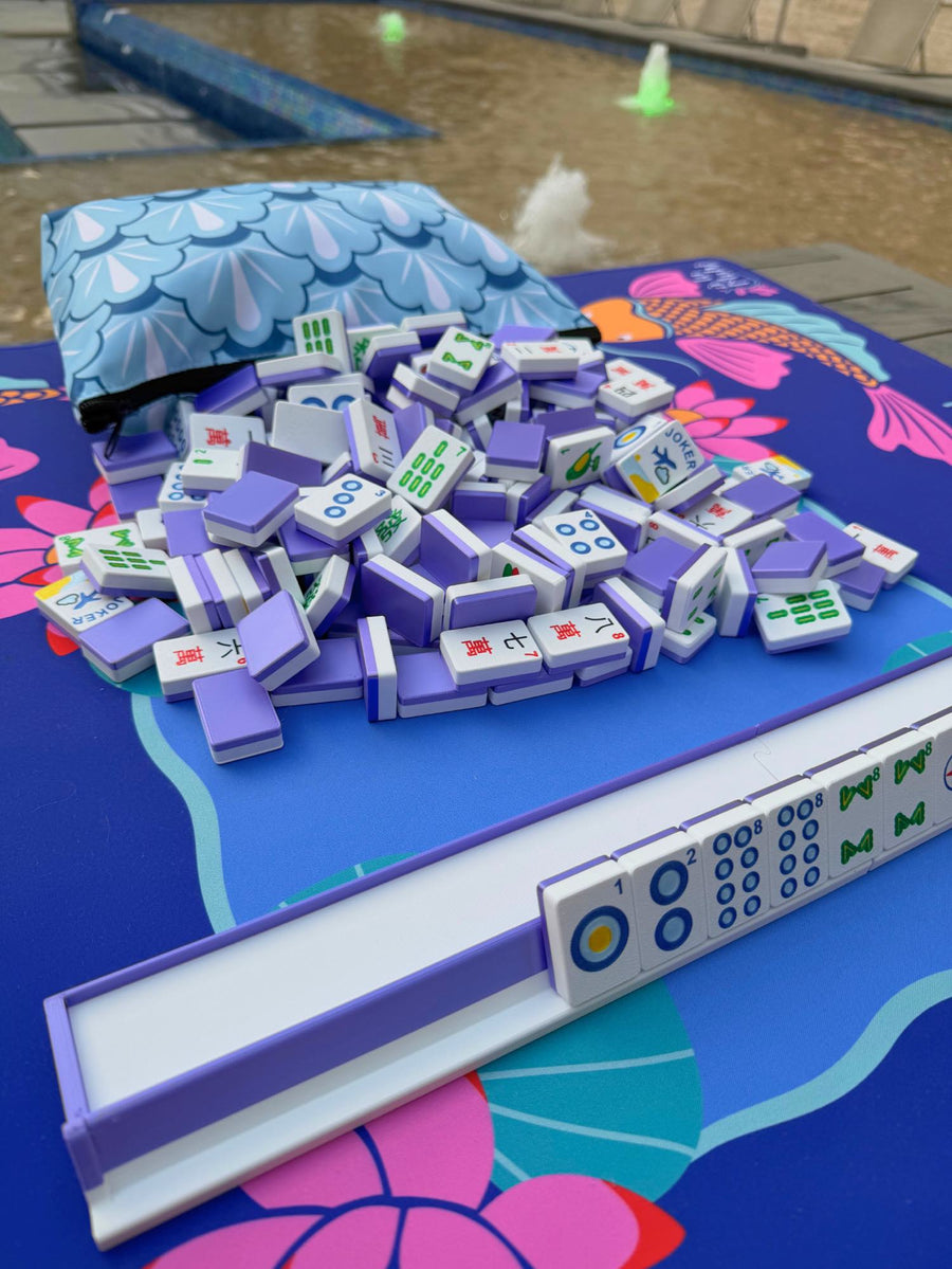 A wider view shows lavender Travel Mahjong Tiles piled beside their open pouch, the mat's rack and pusher visible below.