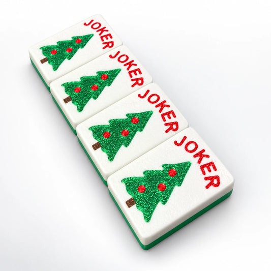 Four Spools mahjong joker tiles with sparkly green Christmas trees, red ornaments and red JOKER lettering, white faces with green backs, angled view