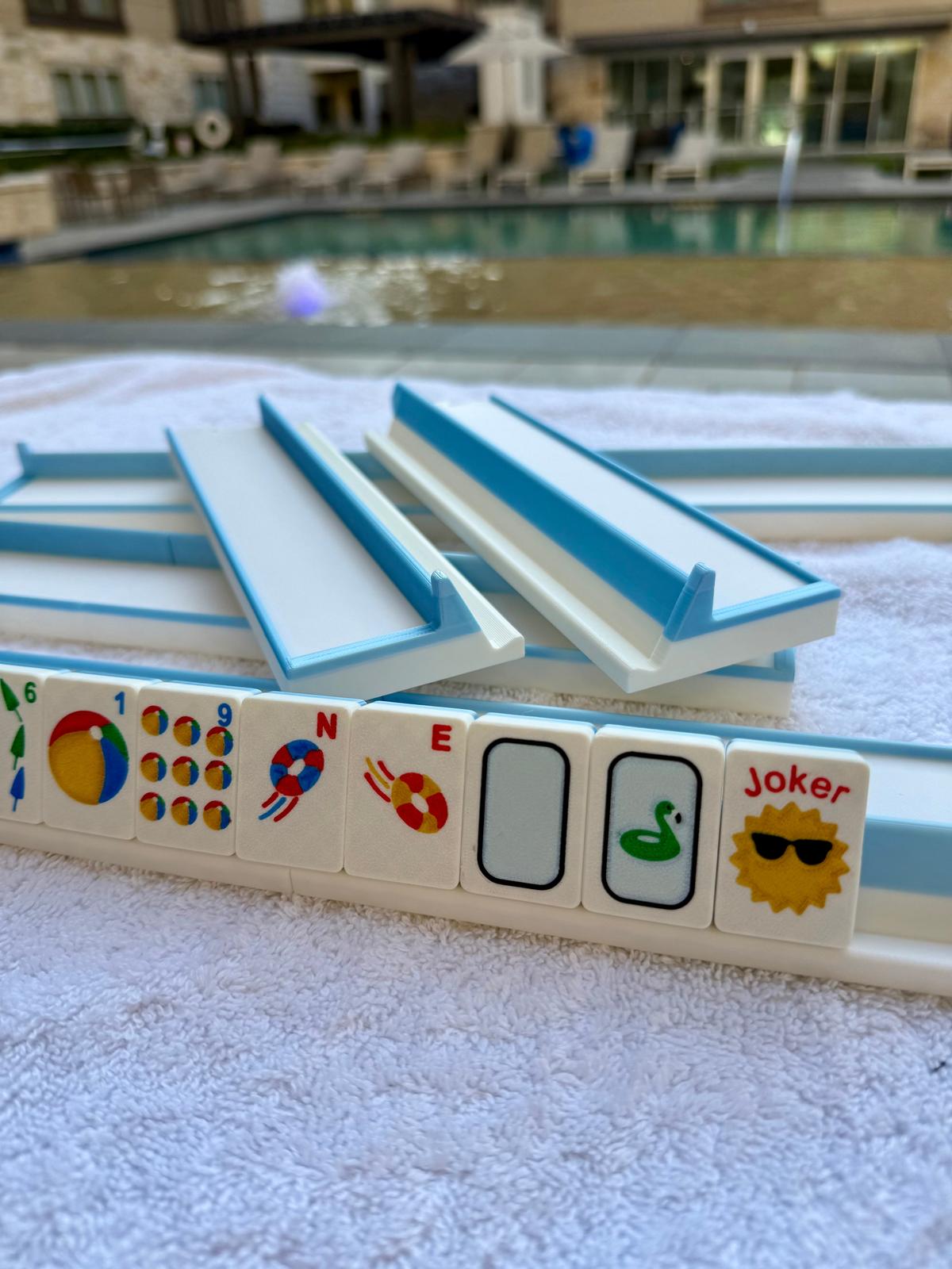 Floating travel mahjong tiles with summer-themed designs and matching blue travel racks on a towel by the poolside, perfect for outdoor and water-friendly mahjong games.