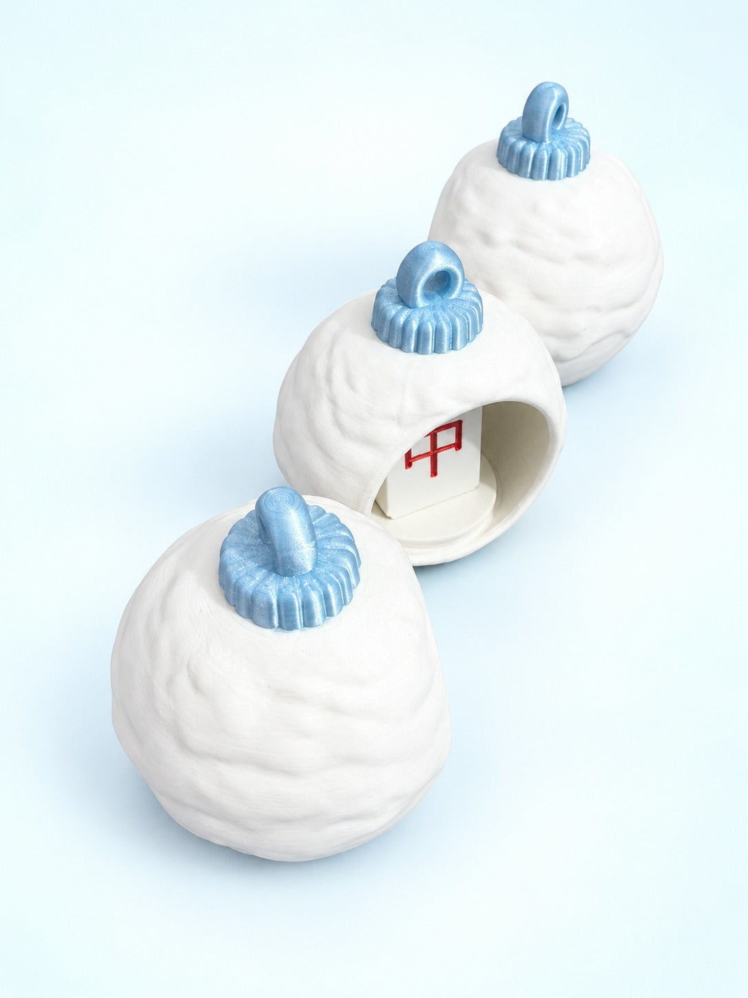 Overhead view of three white mahjong bauble ornaments with pale blue caps and hanging loops