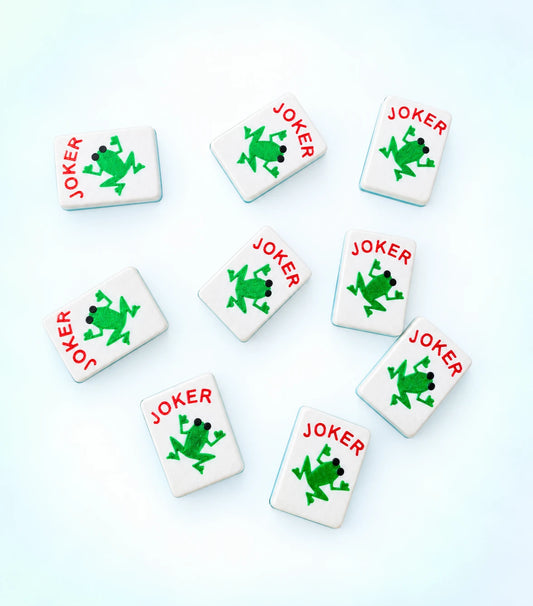 Spools frog joker mahjong tiles, each with a green frog and red JOKER lettering, scattered across a light background