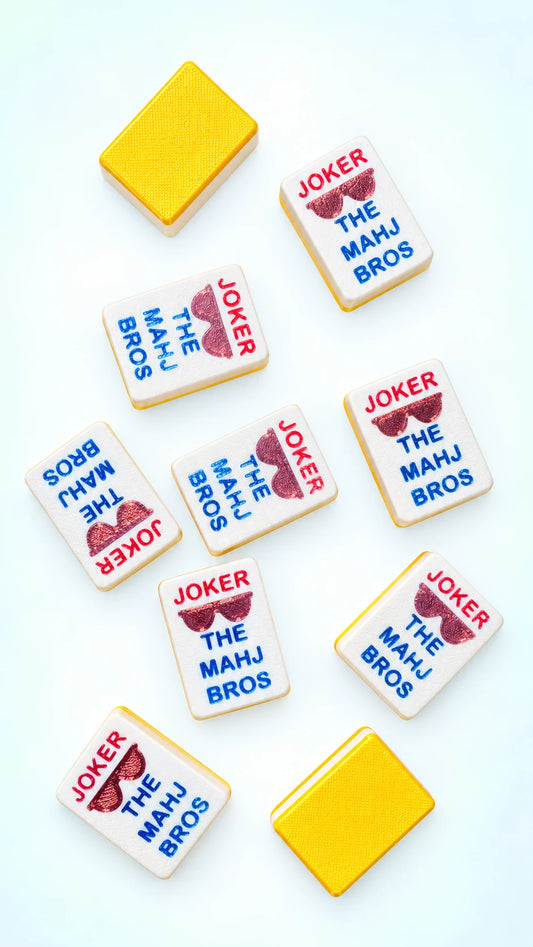 Custom Spools joker mahjong tiles printed with red JOKER, maroon sunglasses, and blue THE MAHJ BROS lettering, beside two yellow tile backs